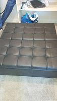 Top view of black faux leather tufted ottoman showing padded cushion top.