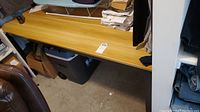 Side angled view of rectangular office table with light brown Formica top showing surface and black metal legs.