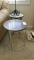 Photo showing gray stone top round side table with silver metal frame and greenish marble top side table with ornate black metal base placed beside a couch.