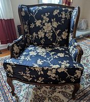 Front view of one armchair showing floral upholstery and carved wooden frame