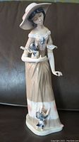 Front view of tall porcelain figurine of a well-dressed young woman holding a dog with another at her hem