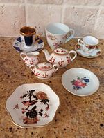 Group photo of all miniature porcelain items: Coalport Indian Tree tea set (teapot, sugar bowl, creamer), Royal Albert Old Country Roses cup and saucer, Marianne's Porcelain miniature cup and saucer, SPAL Porcelanas Portugal painted cup and saucer, two small floral ring dishes