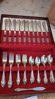 Top view of the wooden flatware box with serrated knives laid out in slots above and forks and spoons below on red felt
