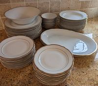 Full set of Kahla dinnerware arranged on kitchen counter showing variety of plates, bowls and platters with gold rims.