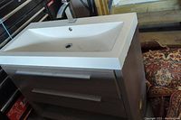 Front angle view showing white rectangular sink on top of dark wood vanity with two drawers and silver handles, placed in storage or garage environment.
