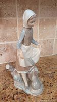 Angled front view of Lladró young woman figurine standing with a rabbit at her feet, holding skirt edges.