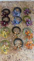 Photo showing 12 glass napkin rings arranged in pairs of various colors with glass flower embellishments.