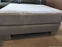 Close-up side view showing soft grey fabric upholstery and sleek silver-colored metal legs.