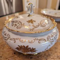 Close-up of the covered candy dish with gold leaf floral and scroll pattern, gold scalloped rim, and handle on lid