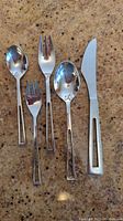 Close-up of individual utensils showing one knife, two spoons and two forks on counter.
