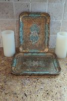 Two wooden Florentine trays displayed vertically and horizontally on a granite countertop with two ivory battery operated candles flanking the trays.
