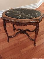 Full view of vintage oval side table with black and brown veined marble inset top on carved wood legs