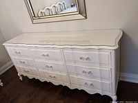 Front view of white painted dresser showing nine drawers and scalloped apron.