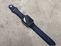 Apple Watch Series 3 42mm with blue sport band lying flat on gray surface, showing front and part of band.