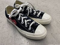 Side view of both shoes showing the red heart logo and white toe caps on black canvas.