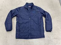 Full view of the navy blue Patagonia men's jacket laid flat on a light surface showing the front side with a zipper and two zip pockets.