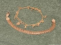 Two sterling silver bracelets laid out flat, one flat link bracelet and one charm bracelet, with a coin for scale.