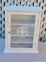 Front view of the white wooden cabinet showing the glass door and overall shape, wrapped in plastic.