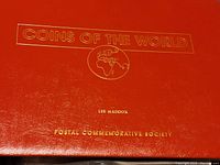 Red binder cover titled 'Coins of the World' by Lee Maddox, Postal Commemorative Society.