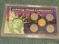 Front side of the hard plastic case showing five Liberty Head coins with a purple background featuring Statue of Liberty and city skyline with 'Liberty Head Collection' text.