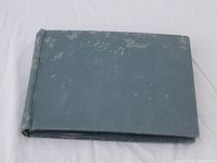 Dark hardcover postcard album with worn cover and faint embossed text.