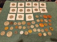 Photo showing a total of 53 coins, 15 quarters in holders, and various loose domestic and foreign coins of different sizes and metal compositions arranged on fabric.