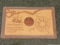 Top view of entire hard case with coin centered on background showing ship and compass graphics.