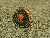 Close-up of ring face showing turquoise inlay with black matrix and central coral stone cabochon, surrounded by twisted rope silver bezel