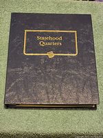 Black faux leather booklet cover with gold embossed 'Statehood Quarters' text.