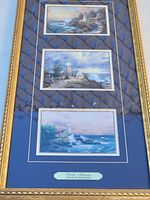 Full view of the three coastal prints by Thomas Kinkade framed together with an ornate gold-tone frame and blue matting.