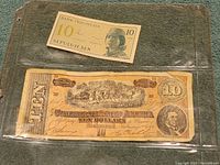 Photo showing the full 10 Sen Bank Indonesia note and partially the Confederate States 10 Dollar bill in plastic protective sleeve