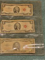Three vintage US currency notes inside a transparent protective binder sleeve, showing two $2 bills and one $5 bill, all Series 1963.