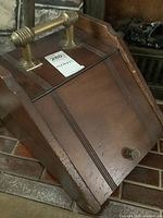 Front view of antique wooden ash bin with brass handle and decorative lines on wood surface. Visible label with dimensions 12x16x12.