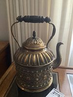 Front view of the ornate brass samovar showing the embossed floral and bead designs on the body and lid, wooden handle, and spout.