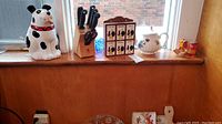 Full lot view showing dog cookie jar, knife block with knives, wooden spice rack, Sadler teapot, and ceramic salt and pepper shakers shaped like birds on a wooden surface by a window.