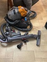 Dyson Stowaway DC21 vacuum unit with clear dust canister, flexible hose, and attached main wand laid flat on tiled floor.