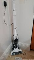 Full length view of the upright Eureka vacuum cleaner plugged into the wall showing overall body and cord.