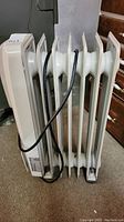 Side view of white radiator heater showing five vertical metal fins and attached power cord.