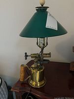 Lamp showing front profile with green shade, brass base, wooden handle, and electrical cord visible on side.