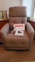 Front view of beige Viva lift chair with remote, instruction manual and paperwork on seat