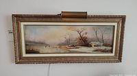 Full view of the framed oil painting with attached picture light showing winter skating scene
