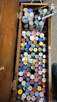 Overhead view of wooden box filled with rows of small paint bottles of various colors