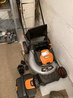 Side view of the grey, black, and orange Worx rechargeable lawn mower with battery compartment visible and folded handlebar.