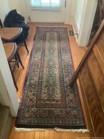 Full view of Gabbeh runner rug laid on wood floor between furniture and front door, showing overall wear and shape.