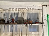 Shelf with multiple small retro tools arranged side by side, including chisels, hand drills with wooden handles, screwdrivers, hooking tools, an oil can, and safety glasses.