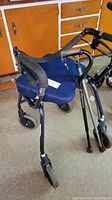 Full view of purple walker with blue seat cushion and foam-handled grips showing hand brakes and wheels, positioned upright.