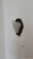 Single wall lamp mounted on wall, bronze metal base with frosted glass shade shaped like shell