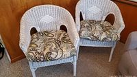 Two white wicker bucket chairs with patterned cushions, showing frayed wicker and worn condition.