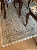 View of the full rug under dining chairs showing overall pattern and wear.