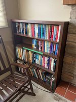 Front view of the wooden bookcase packed with books, showing three fixed shelves and wear spot on top.